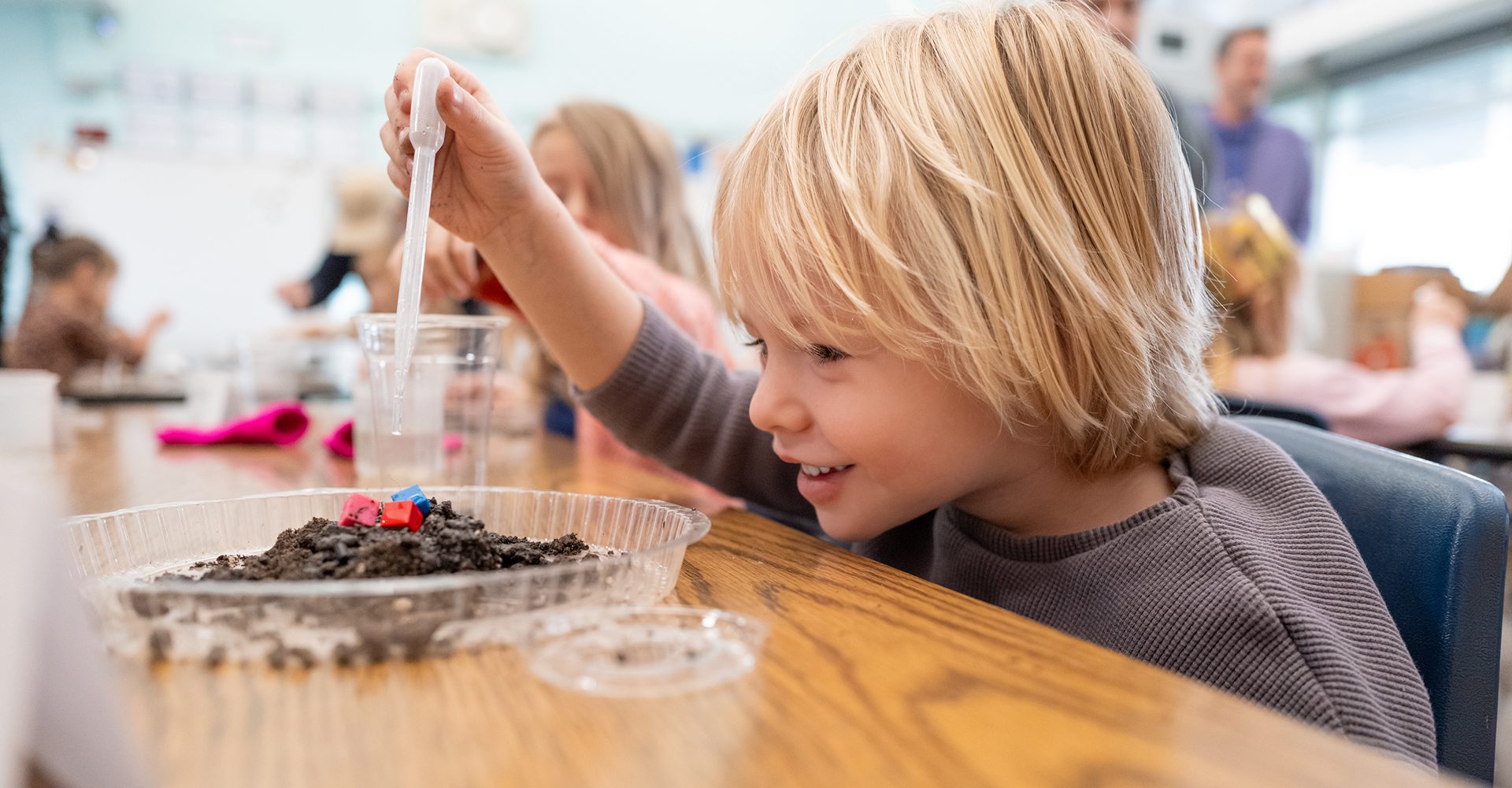 A child excitedly watches insects in a plastic container outdoors.