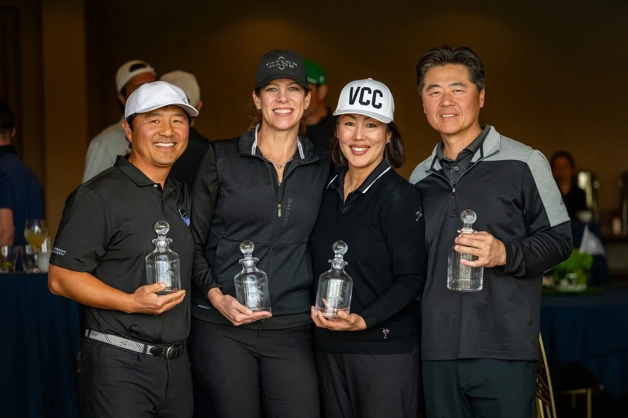Group of four smiling golfers holding trophies.