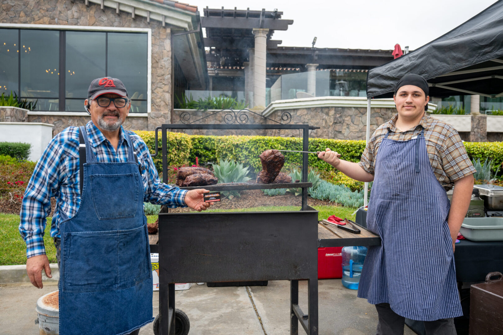 Two men grilling meat outdoors at event.