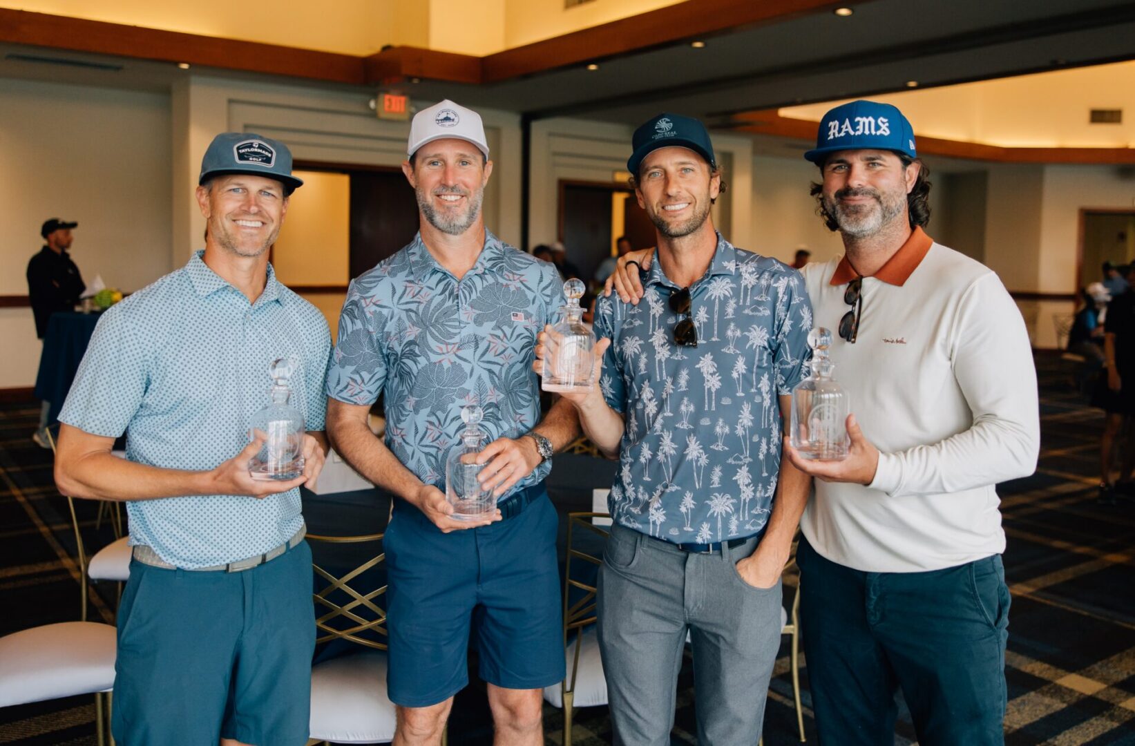 Four men holding trophies in a celebration.