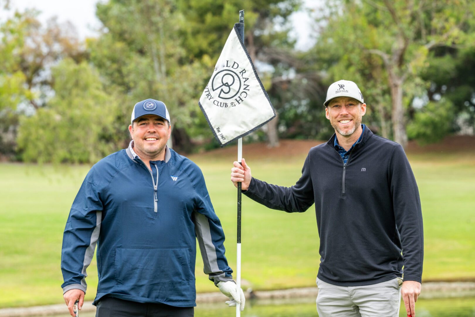 Two golfers smiling with a club flag.
